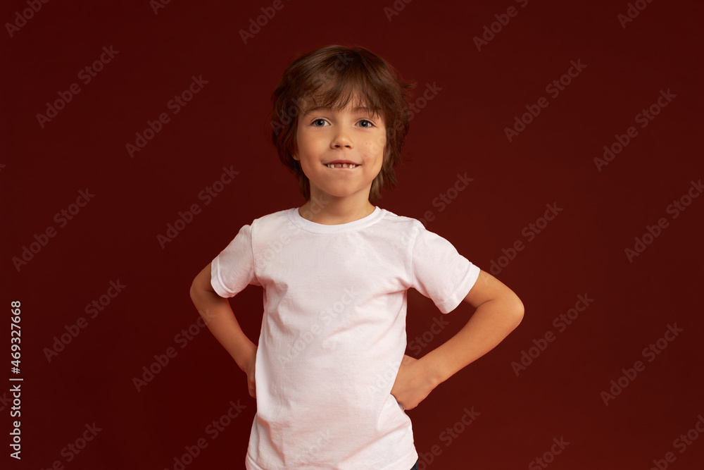 Indoor image of happy good-looking Caucasian brunette kid keeping hands on waist, pretending being big boss, having toothy smile, showing new front permanent teeth, isolated on red Indoor image of happy good-looking Caucasian brunette kid keeping hands on waist, pretending being big boss, having toothy smile, showing new front permanent teeth, isolated on red