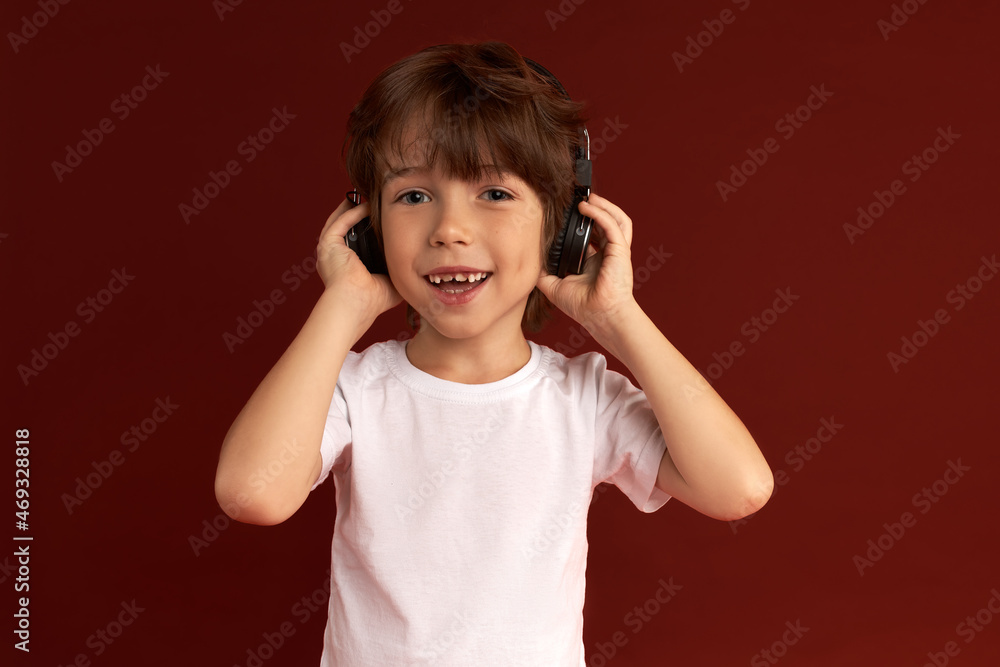 Close-up studio shot of adorable casually dressed cool brunette kid in stylish wireless headphones, listening to favorite music, enjoying sounds, beats, rhythm. Children and technology Close-up studio shot of adorable casually dressed cool brunette kid in stylish wireless headphones, listening to favorite music, enjoying sounds, beats, rhythm. Children and technology