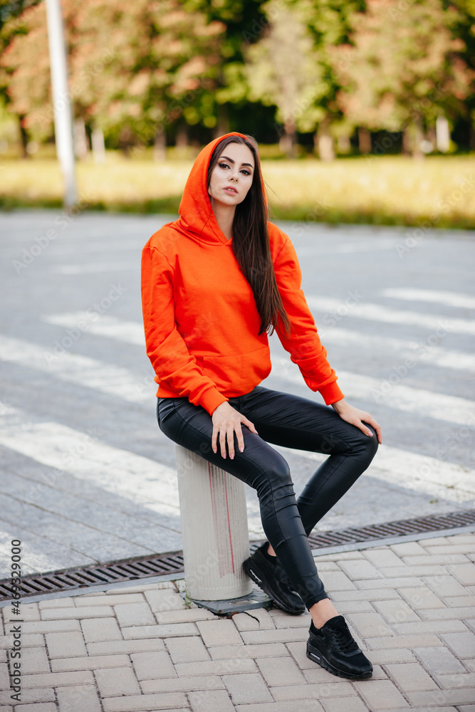 Fototapeta premium Ultra-fashion concept. Young woman of fashion wearing orange sweater and posing over orange bricks urban background. Street style. businesswoman. fashionable accessories.