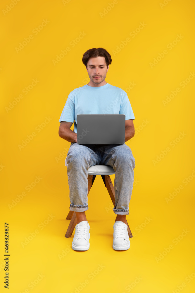 Serious guy using laptop sitting on chair at studio