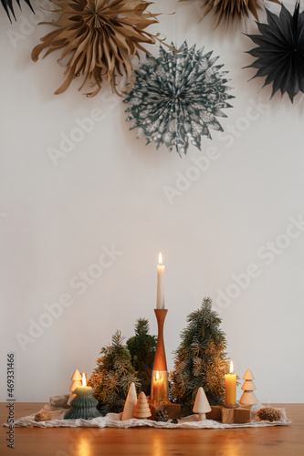 Stylish christmas candles and trees decorations on wooden table against sweden paper stars