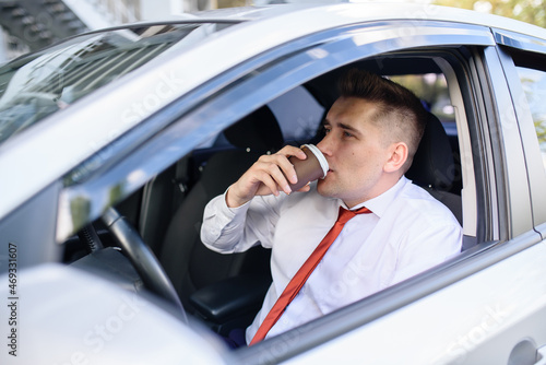 A man in a suit drinks coffee in the car