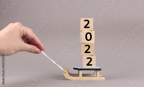 Hand pulls toy wooden sled with wooden cubes with numbers 2022 on gray background. New year 2022 photo