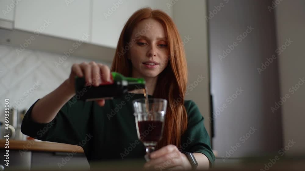 Close-up of attractive young woman pouring alcohol beverage in glass in kitchen with modern light interior. Low-angle view of pretty female drinking wine alone at home. Shooting in slow motion. Close-up of attractive young woman pouring alcohol beverage in glass in kitchen with modern light interior. Low-angle view of pretty female drinking wine alone at home. Shooting in slow motion.