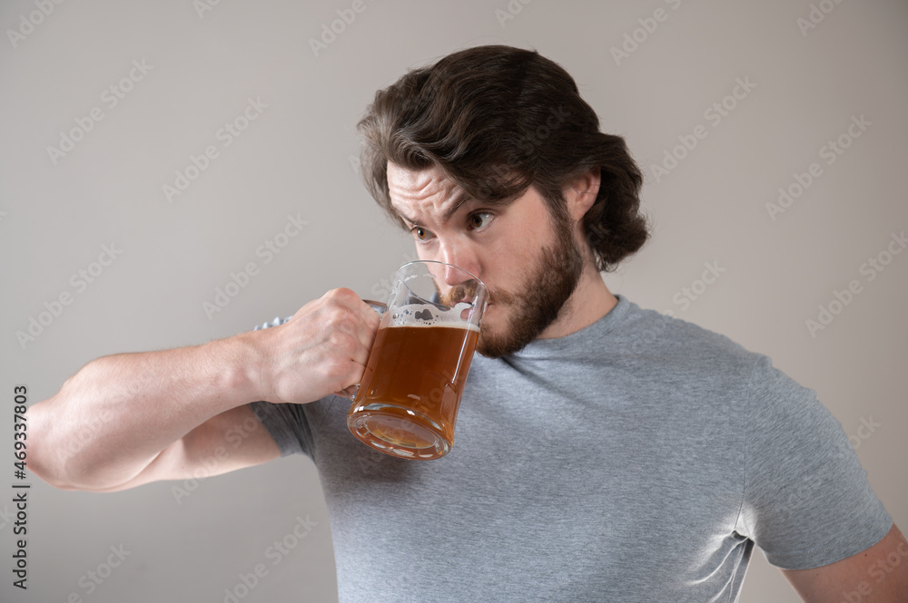 bearded man drinking beer with a big mug on a gray background bearded man drinking beer with a big mug on a gray background