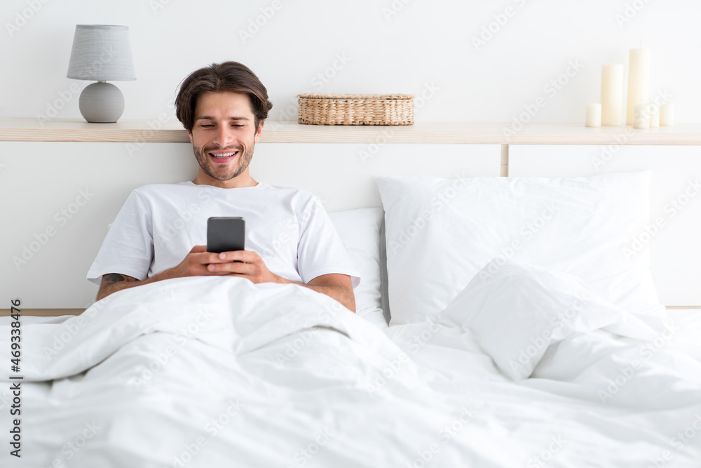 Cheerful attractive millennial european guy with stubble play on phone, surfing in internet on smartphone Cheerful attractive millennial european guy with stubble play on phone, surfing in internet on smartphone