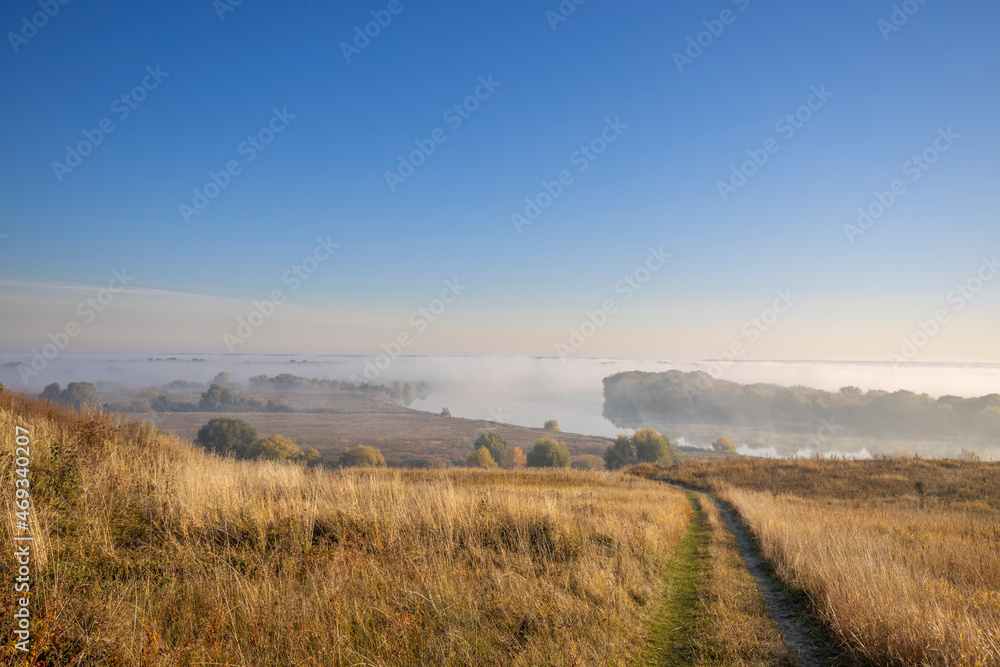 Autumn landscape in the early morning. Fog-covered expanses through which the first rays of the rising sun pass. Trees and hills in the fog. Dawn on a cold autumn morning.