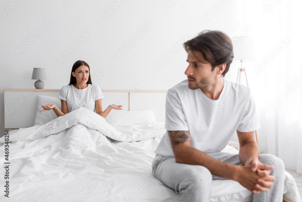 Sad depressed young european husband with stubble looks at screaming wife in bedroom interior, empty space Sad depressed young european husband with stubble looks at screaming wife in bedroom interior, empty space