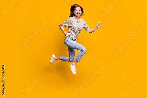 Full length body size view of nice thin funny cheerful girl jumping running fast speed isolated over bright yellow color background © deagreez