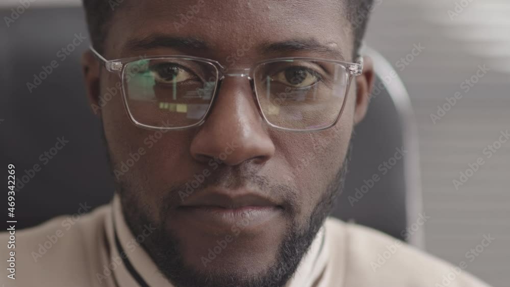 Slowmo close-up of young African-American programmer looking at computer screen with program codes reflecting in his eyeglasses Slowmo close-up of young African-American programmer looking at computer screen with program codes reflecting in his eyeglasses