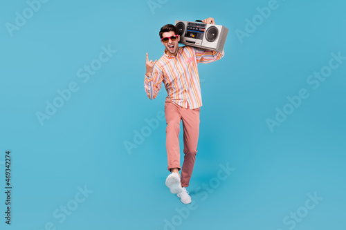 Full length photo of young man happy positive smile show fingers rock sign retro song boombox isolated over blue color background