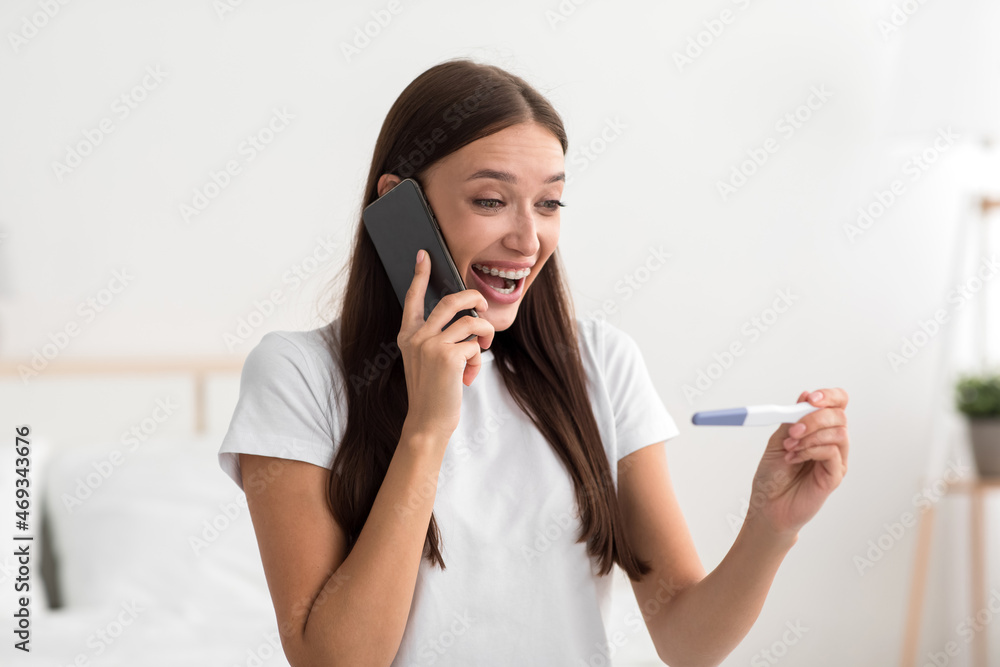 Cheerful excited pretty millennial european woman hold pregnancy test in bedroom interior and calling to boyfriend Cheerful excited pretty millennial european woman hold pregnancy test in bedroom interior and calling to boyfriend