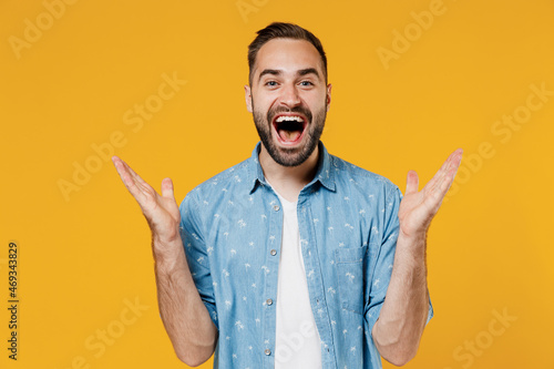Tablou pe pânză Young happy joyful fun surprised overjoyed excited caucasian man 20s wear blue shirt white t-shirt spread hands scream isolated on plain yellow background studio portrait