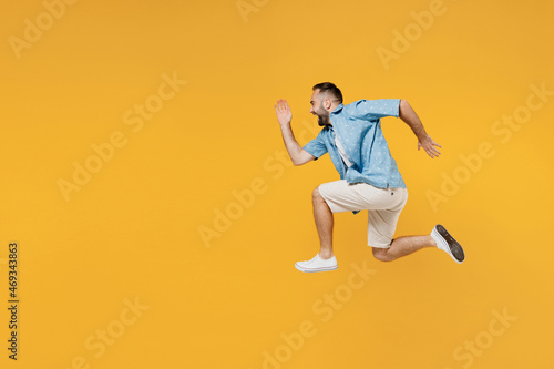 Full body side view young smiling sporty happy caucasian man 20s in blue shirt white t-shirt run fast jump high hurry up isolated on plain yellow background studio portrait. People lifestyle concept.