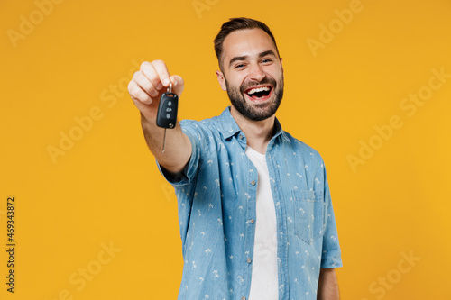 Obraz na płótnie Young smiling happy caucasian man 20s wearing blue shirt white t-shirt hold give car key fob keyless system look camera isolated on plain yellow background studio portrait
