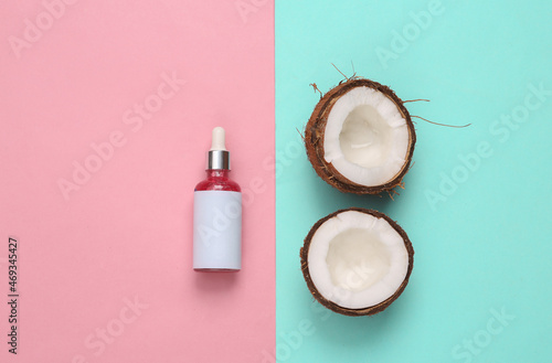 Bottle of face serum and coconut on a blue-pink background. Natural cosmetics concept