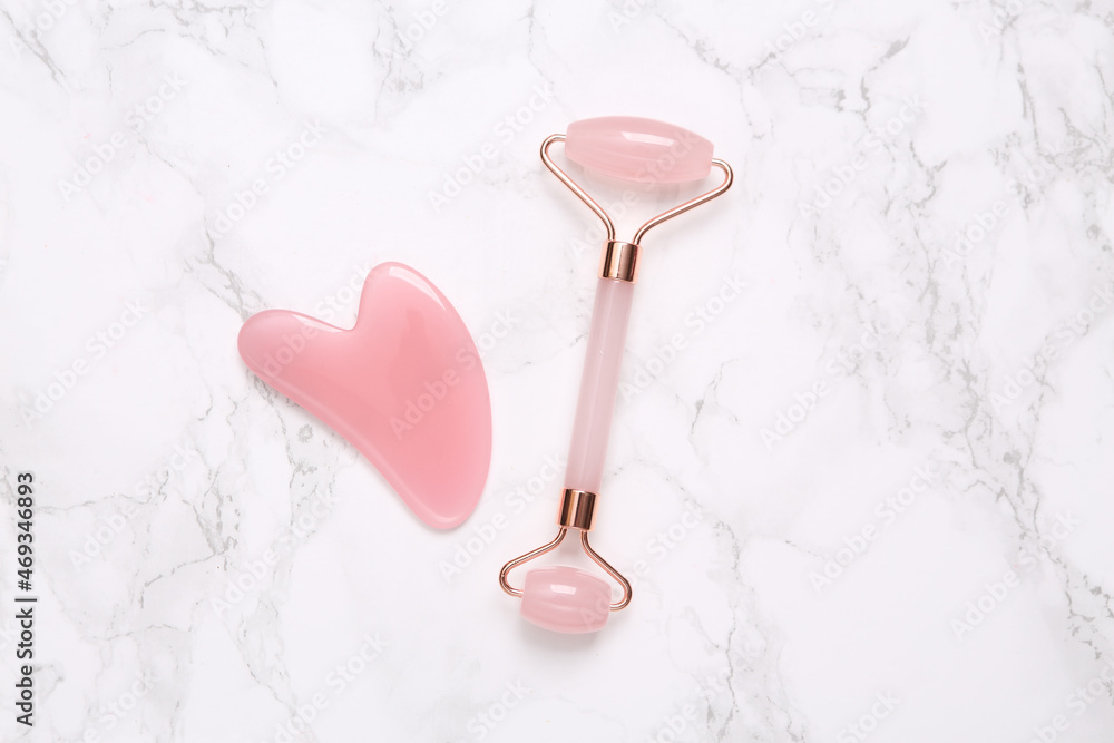 Face roller and gua sha stone massager on marble background Face roller and gua sha stone massager on marble background