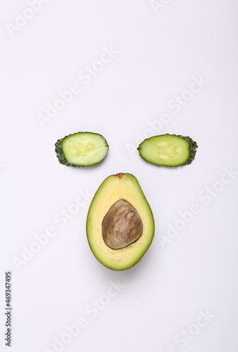 Creative composition of cucumber and avocado slices in the shape of face on white background