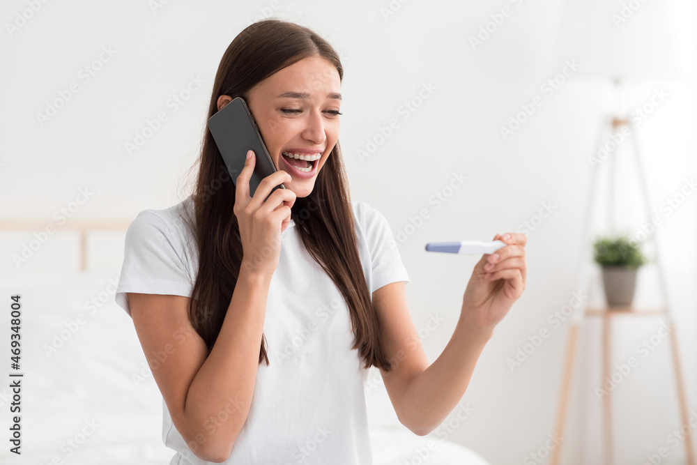 Shocked glad millennial caucasian lady hold positive pregnancy test in bedroom interior and calling her husband Shocked glad millennial caucasian lady hold positive pregnancy test in bedroom interior and calling her husband