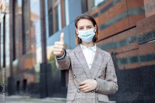 Woman with medical mask showing thumb up in the city