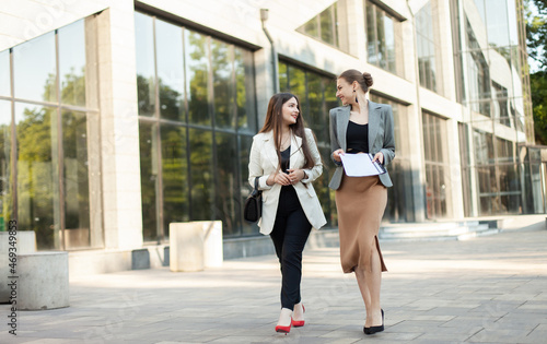 Two business women friends communicate while walking in the city on the background of a business building