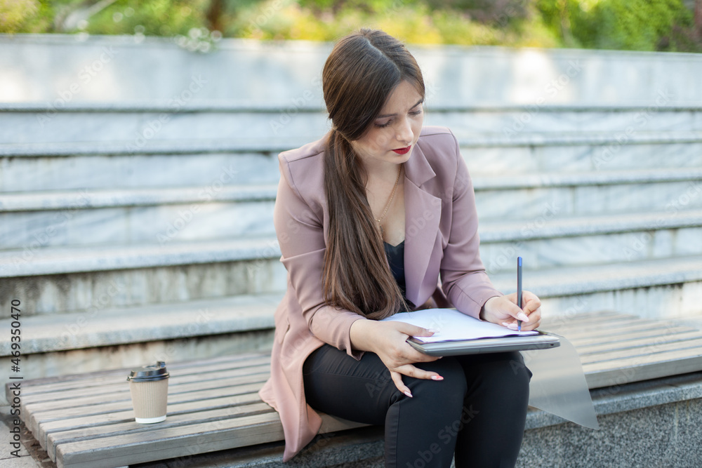 Obraz premium Business woman writes important information on a sheet of paper while sitting on bench in park