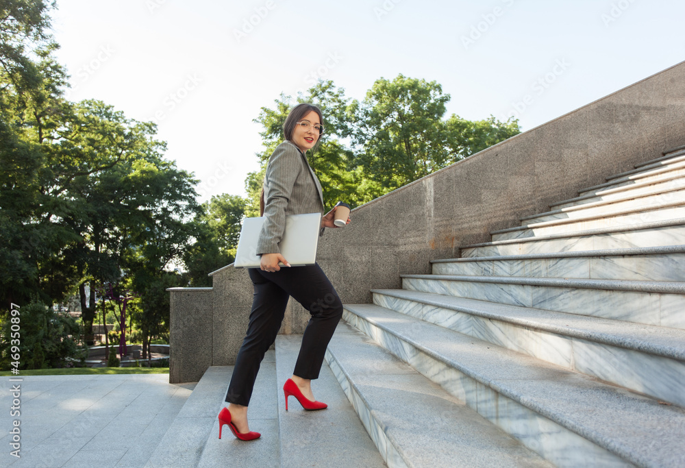 Business woman with laptop and a cup of coffee on the go climbs the stairs up Business woman with laptop and a cup of coffee on the go climbs the stairs up