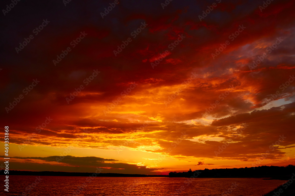 Evening cloudscape in twilight. Ruddy horizon sky and river. Morning fiery orange sunrise in summer dawn. Red cloudy sunset above lake at dusk. Bloody sky above reflective water surface waves in wind
