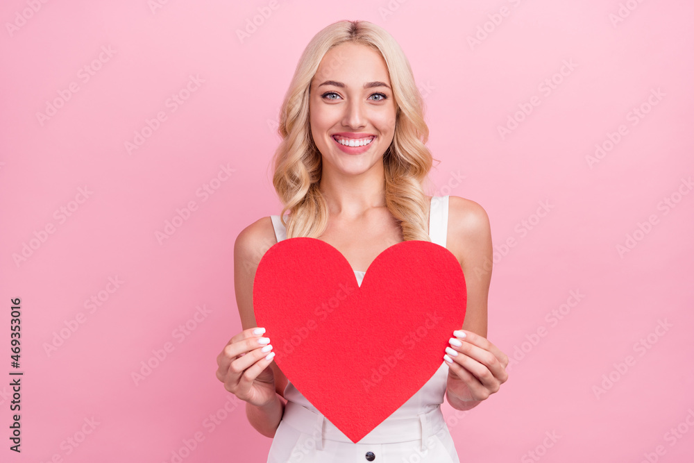 Photo of pretty adorable young lady wear white overall smiling holding large red heart isolated pink color background Photo of pretty adorable young lady wear white overall smiling holding large red heart isolated pink color background