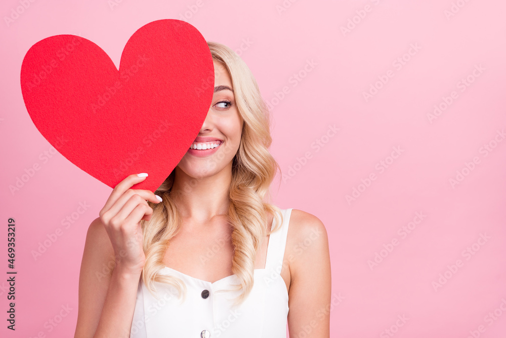 Photo of shiny pretty young lady wear white overall smiling large red heart close eye looking empty space isolated pink color background Photo of shiny pretty young lady wear white overall smiling large red heart close eye looking empty space isolated pink color background