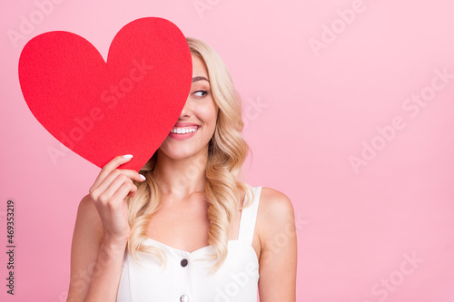 Photo of shiny pretty young lady wear white overall smiling large red heart close eye looking empty space isolated pink color background © deagreez