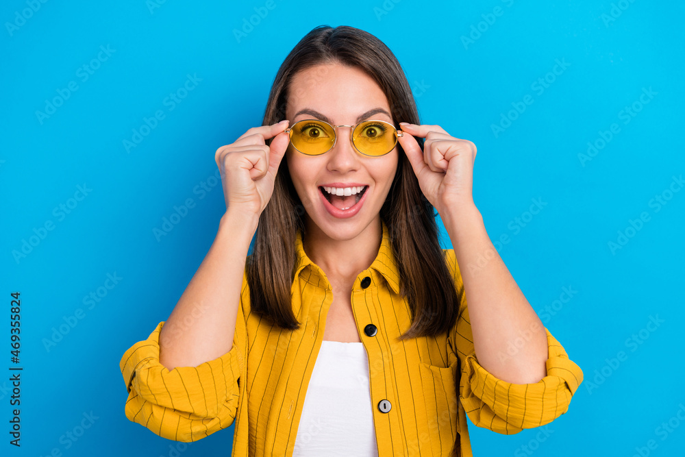 Photo of young excited girl amazed surprised omg wow reaction sunglass news isolated over blue color background Photo of young excited girl amazed surprised omg wow reaction sunglass news isolated over blue color background