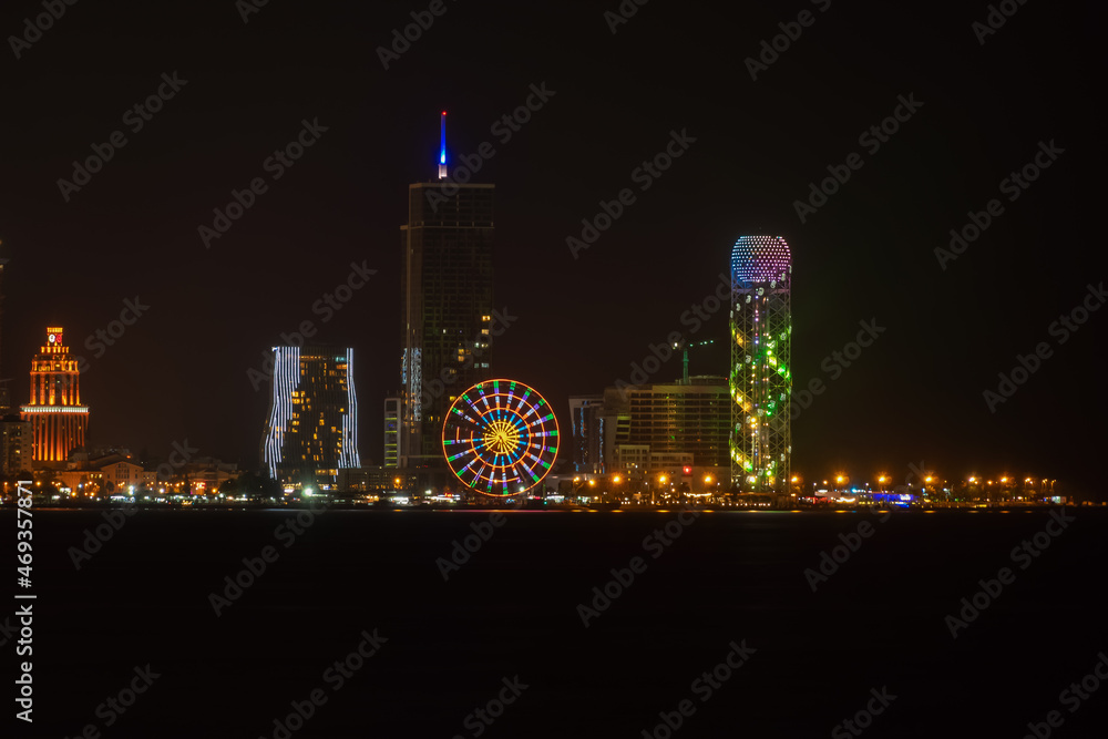 View from the sea to the Batumi embankment on a dark night. Illumination of buildings, Ferris wheels, Batumi embankment, Adjara at night