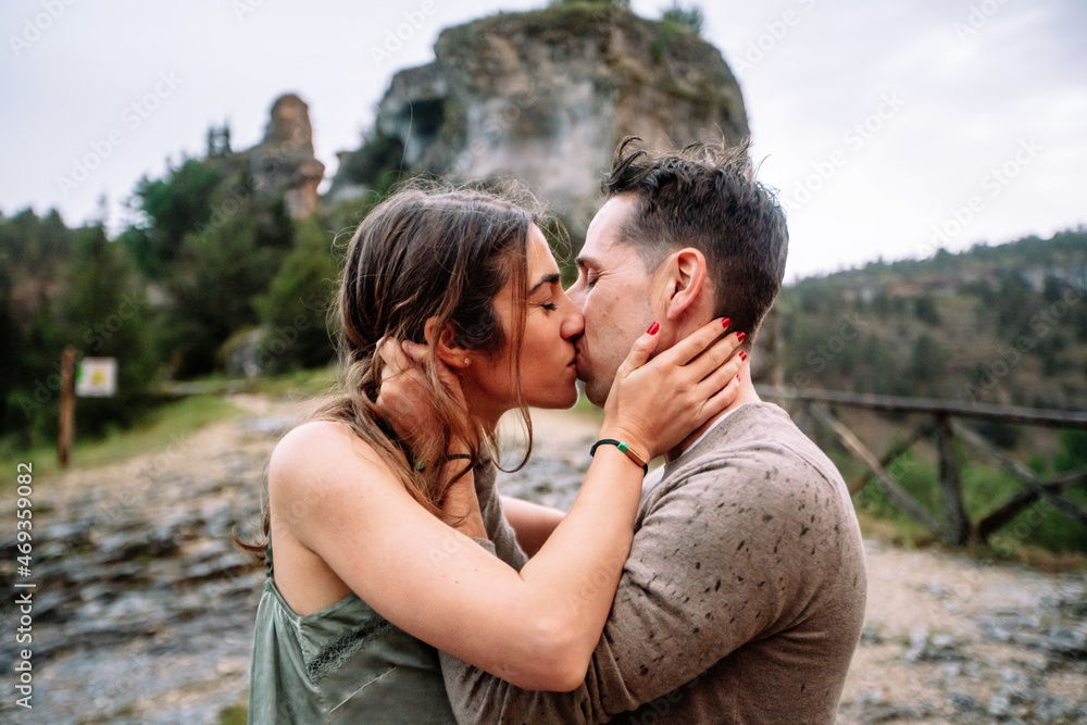 Side view of caucasian couple in love kissing and hugging. Horizontal view of couple kissing with love outdoors in nature background. People and travel concept.