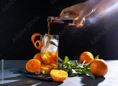 Chinotto drink in the glass with ice and fruits on the grey table photo