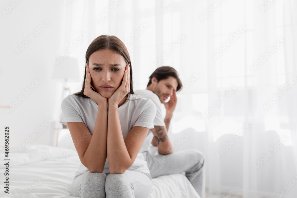 Disappointed young caucasian lady sits on bed, ignores offended man Disappointed young caucasian lady sits on bed, ignores offended man