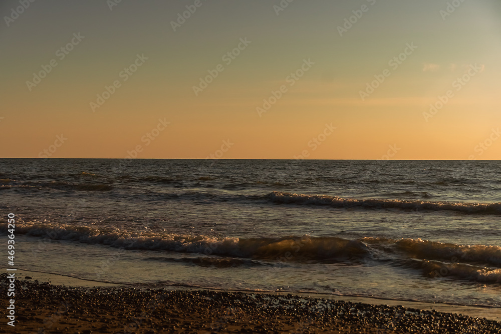 Beautiful golden sunset on the sea with waves and a sandy beach and pebbles. Beautiful nature background. Holiday by the sea
