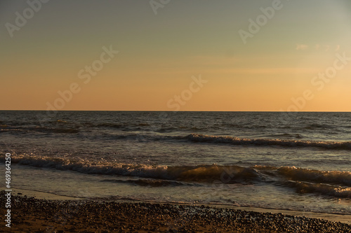 Beautiful golden sunset on the sea with waves and a sandy beach and pebbles. Beautiful nature background. Holiday by the sea