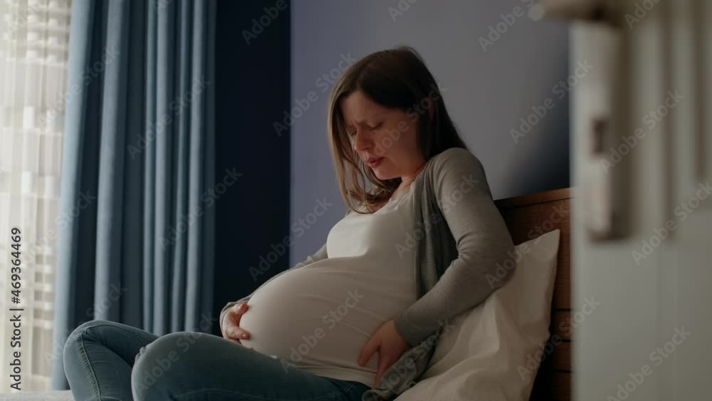 Pregnant woman with big belly sitting in the bedroom, contractions begin, she feels pain. Last month's pregnancy, starting of childbirth. Pregnant woman with big belly sitting in the bedroom, contractions begin, she feels pain. Last month's pregnancy, starting of childbirth.