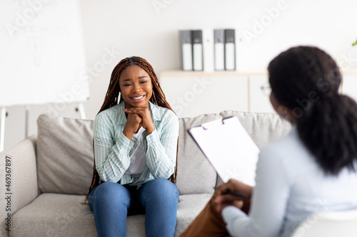 Successful psychotherapy. Millennial female client having session with psychologist, smiling, sitting on couch at clinic photo