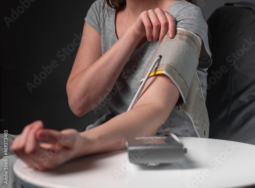 Blood pressure checking by young woman, putting on cuff on arm at home at night.