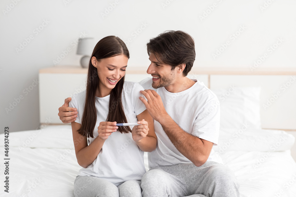 Cheerful young european male and female holds pregnancy test in bedroom interior and rejoice Cheerful young european male and female holds pregnancy test in bedroom interior and rejoice