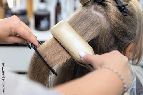 Styling girl's hair with a hot straightening iron.Hair straightener