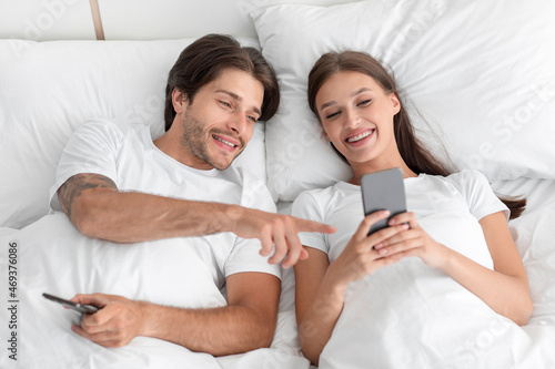 Cheerful young european family looking at phone, chatting in social networks, surfing in internet