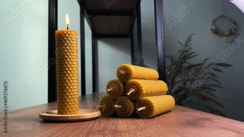 Stylish handmade candle burns on wooden tray near pile of items with honeycomb texture on rustic table in room closeup