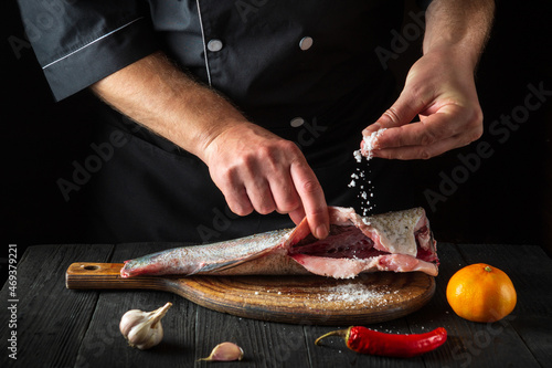 Professional chef prepares fresh fish sprinkling salt. Preparing to cook fish food. Working environment in the restaurant kitchen. photo