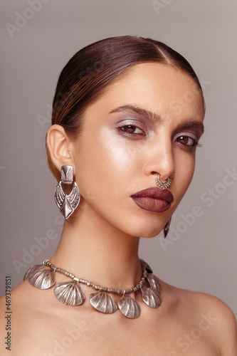 Portrait of a female model, skin care, make-up, with silver bijouterie, looking at camera, over grey background.