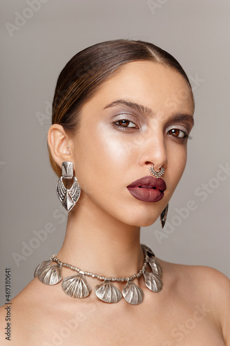 Sensuality woman with suntanned skin, make-up, with silver vintage bijouterie, looking at camera, over grey background.