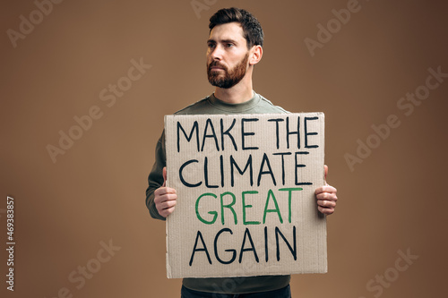 Caucasian serious man holding carton placard with Make the climate great again signs and looking away with proudness. Concept of nature destruction and eco activism