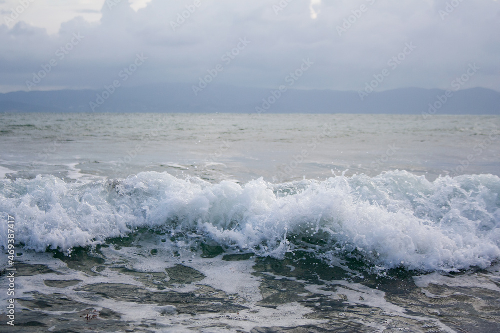 Sea wave below cloudy sky with mountains silhouette on the background Sea wave below cloudy sky with mountains silhouette on the background